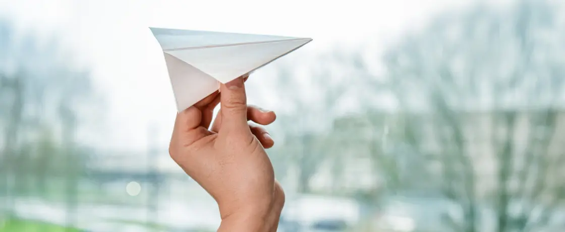 Foto einer Hand, die ein Papierflugzeug wirft