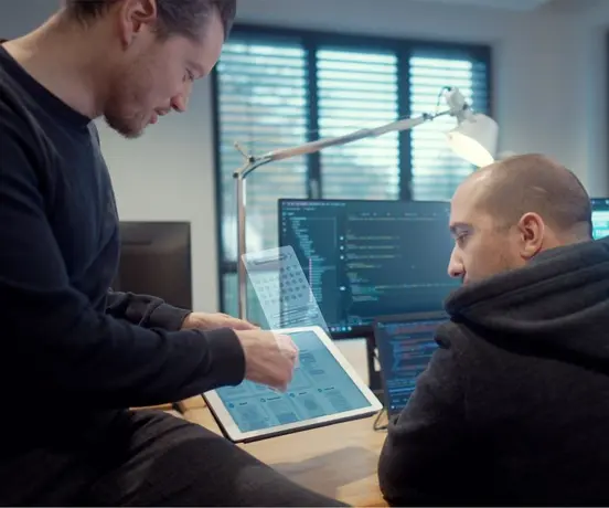 Foto von zwei Programmierern, die mit Tablet und Bildschirmen konzentriert sprechen